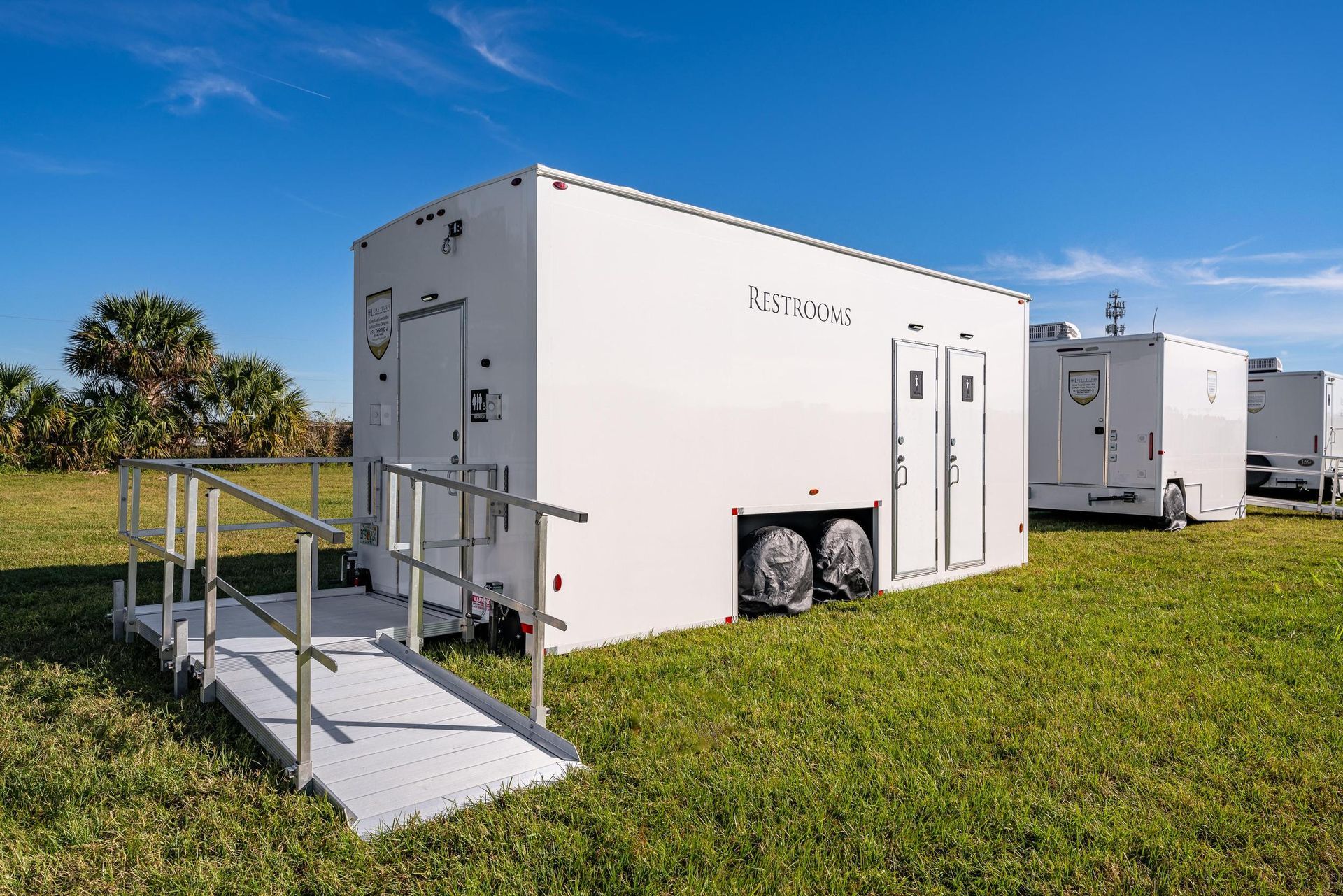 A white trailer with a ramp is parked in a grassy field