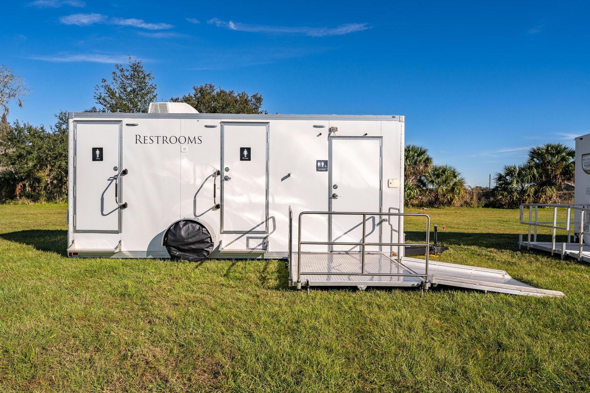 A white trailer with a ramp attached to it is parked in a grassy field