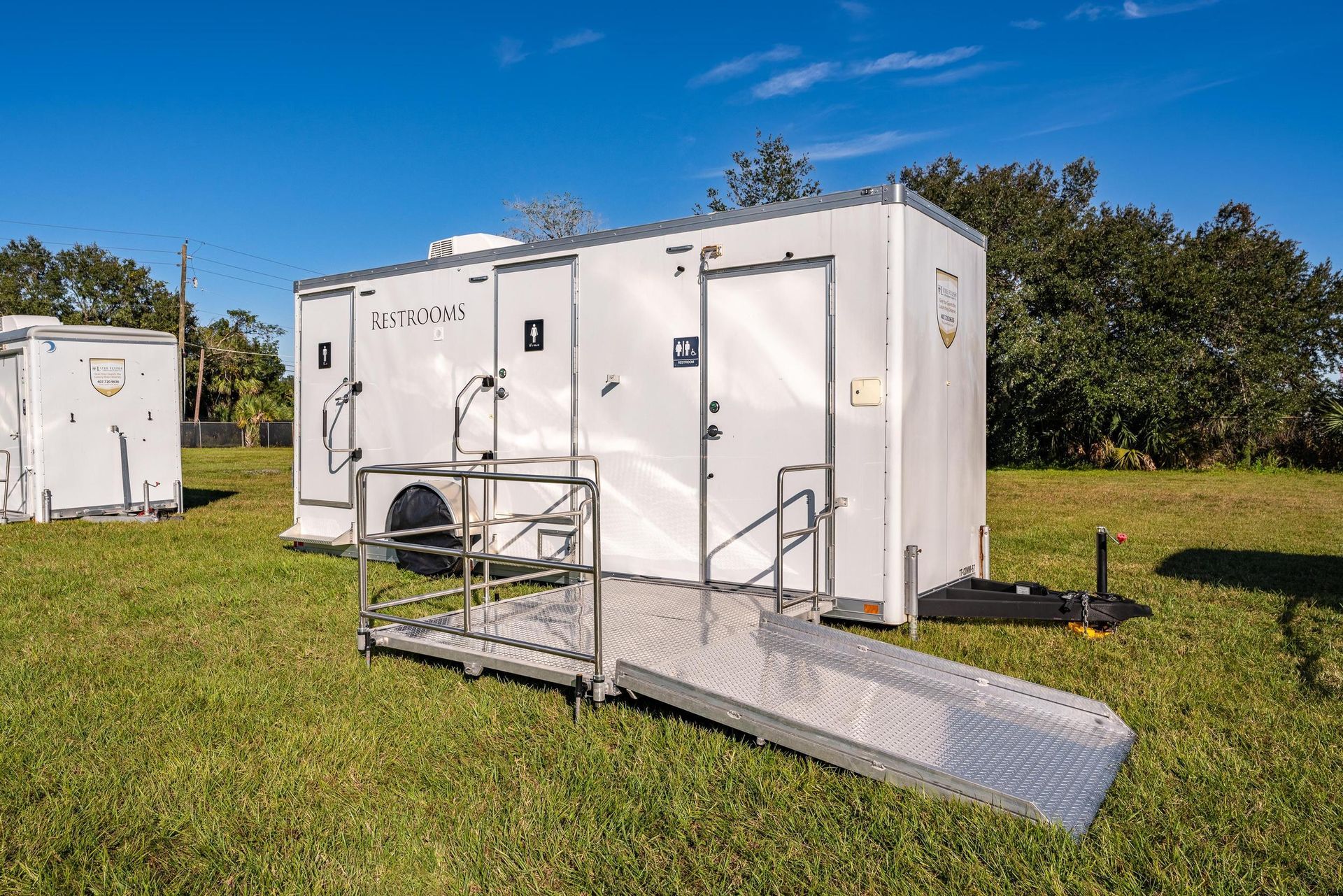 A white trailer with a ramp attached to it is parked in a grassy field