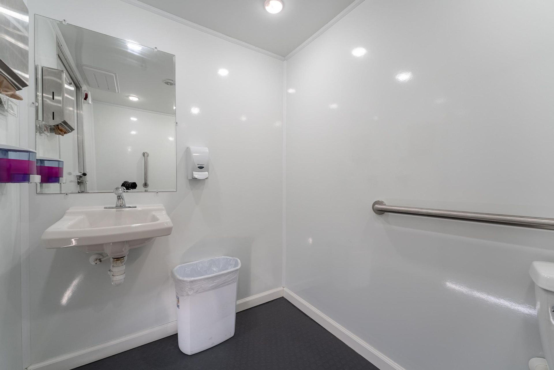 A bathroom with a sink, toilet, mirror, and trash can