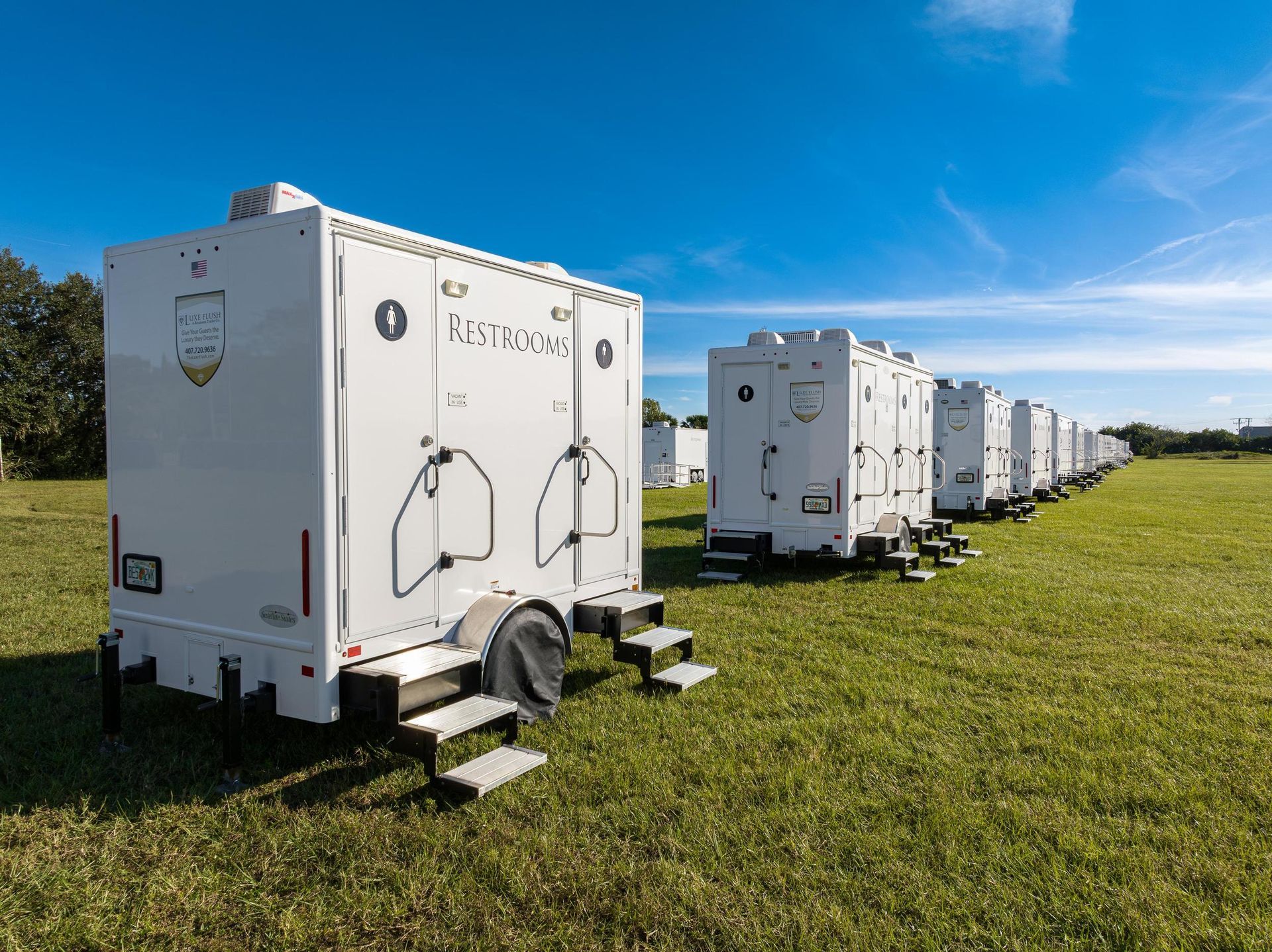 A row of white trailers are parked in a grassy field