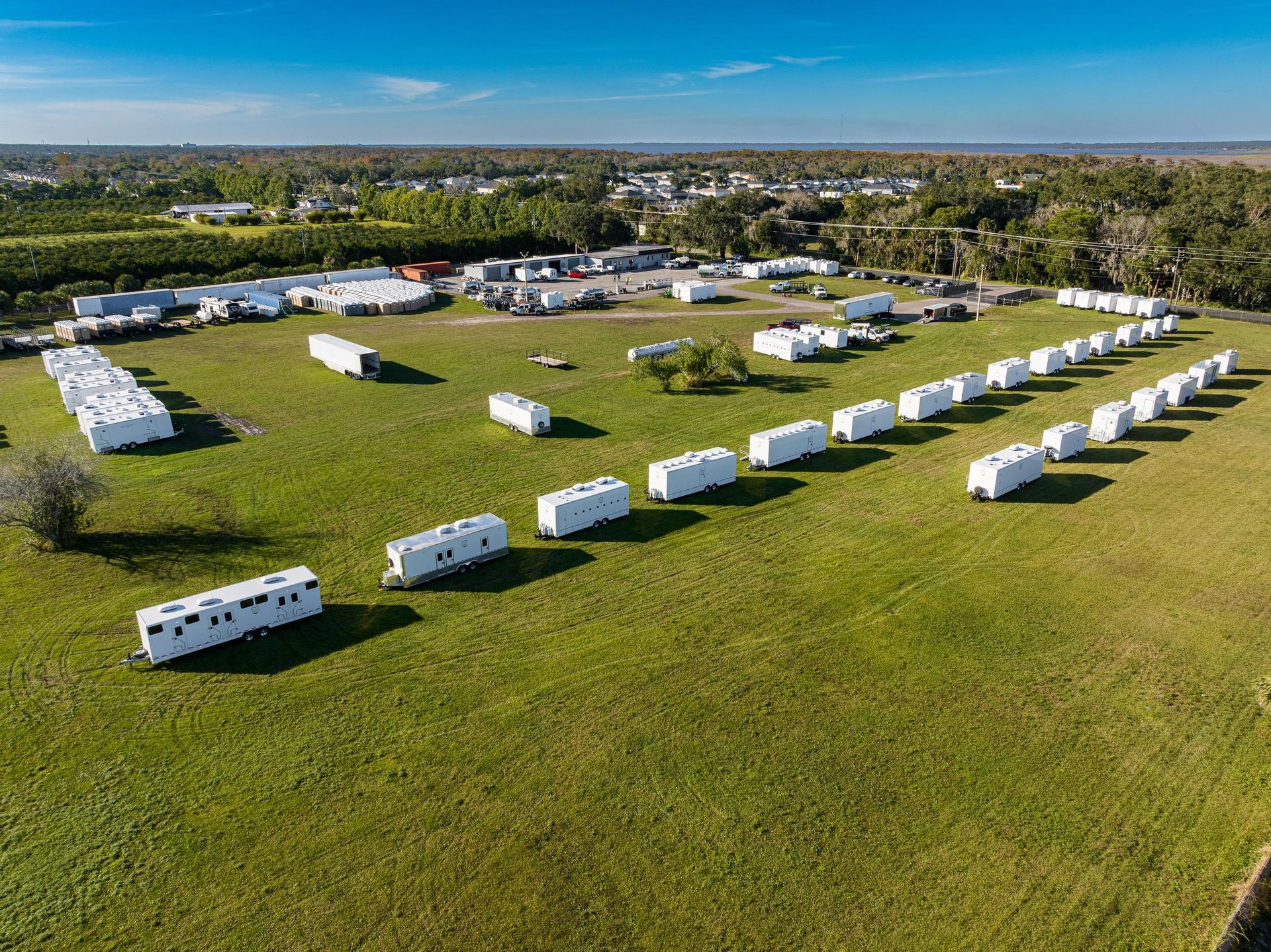 An aerial view of a row of trailers parked in a grassy field