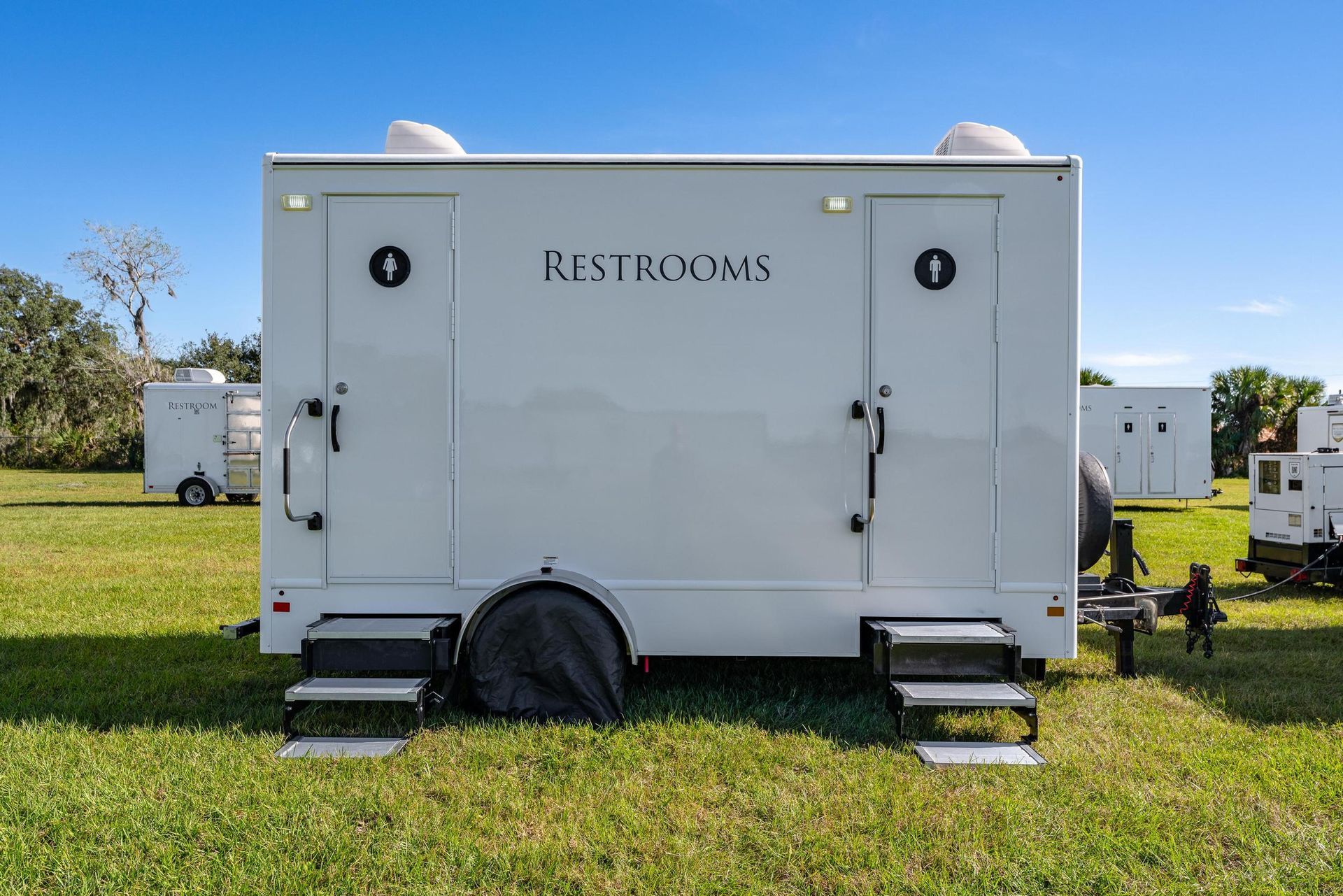 A white trailer with the word restrooms on it is parked in a grassy field