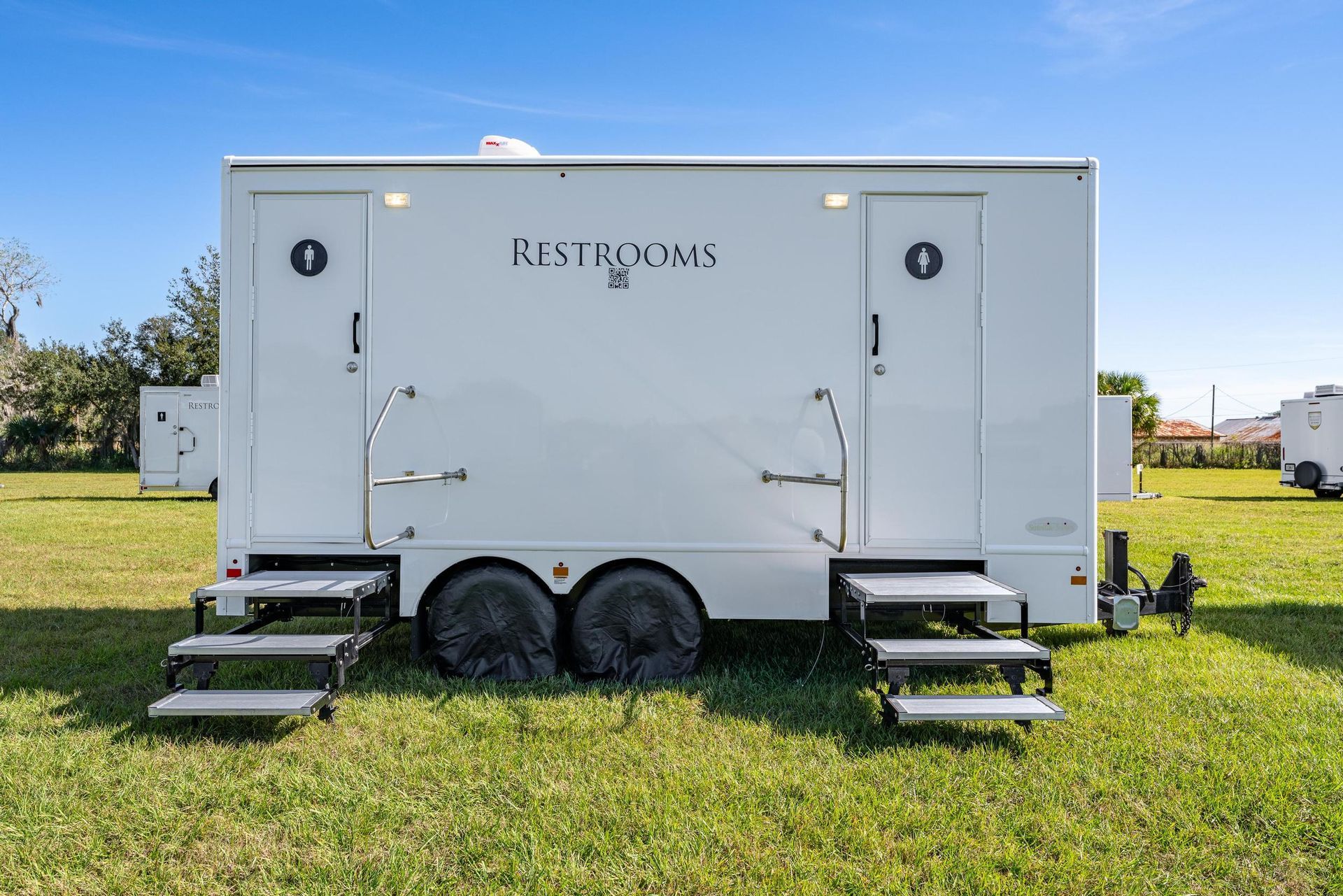 A white trailer with stairs attached to it is parked in a grassy field