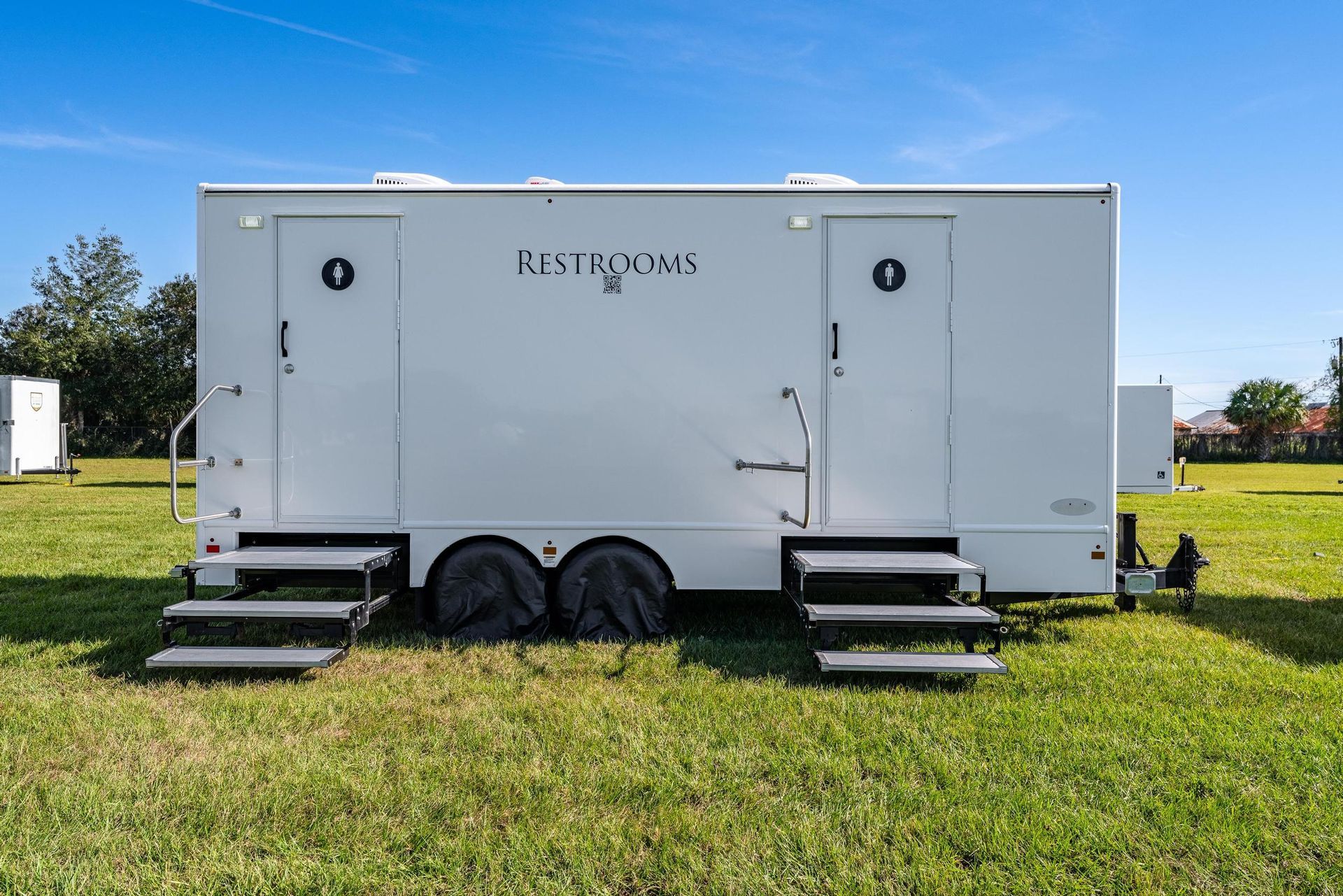 A white trailer with stairs is parked in a grassy field