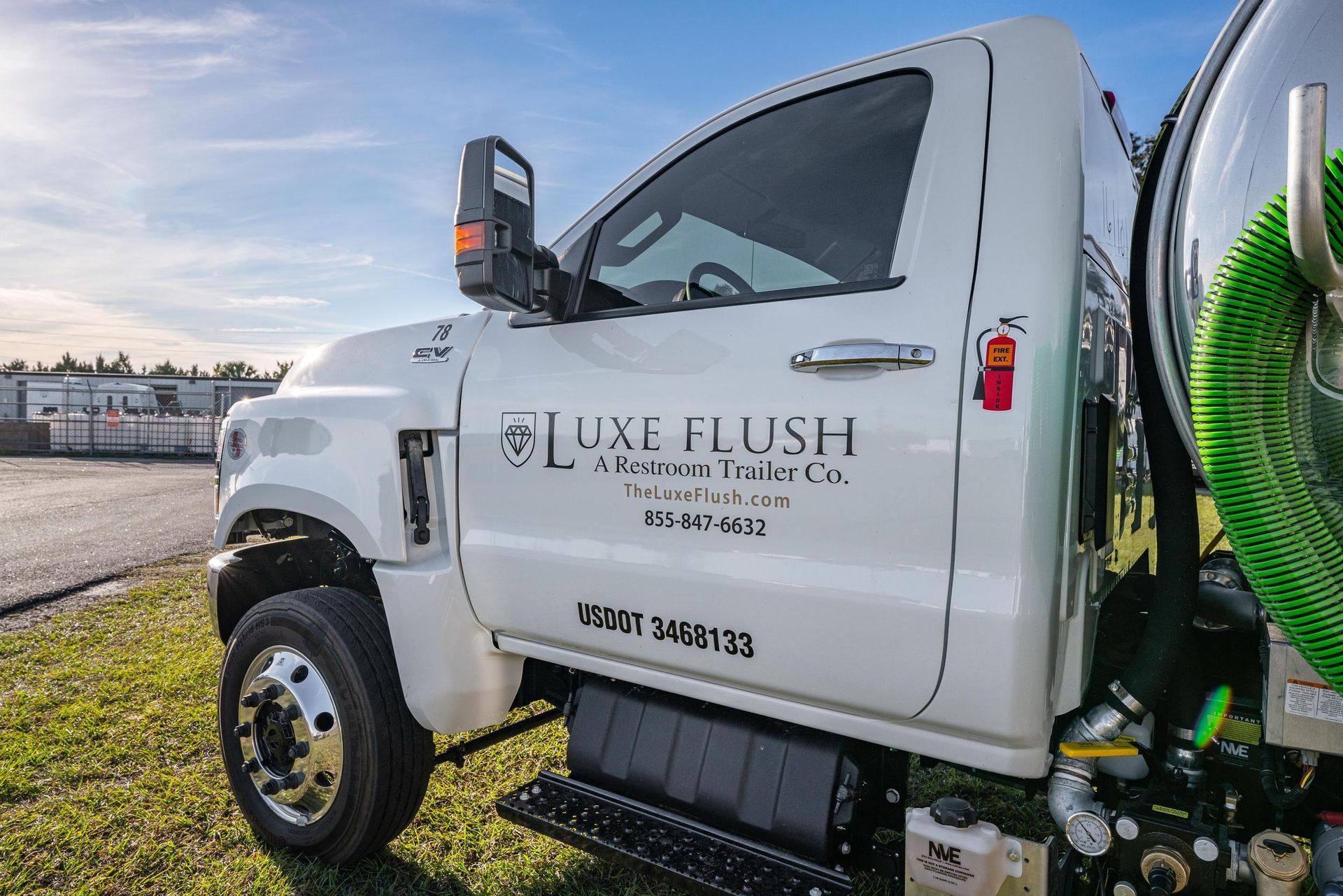 A white truck with a green hose attached to it is parked in a grassy field