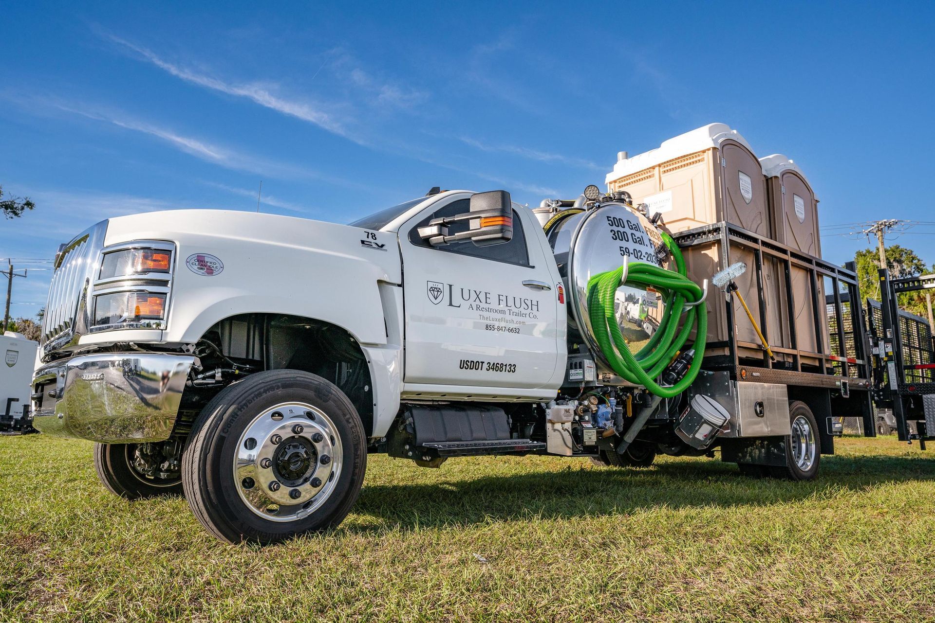 A white truck with a green hose attached to it is parked in a grassy field