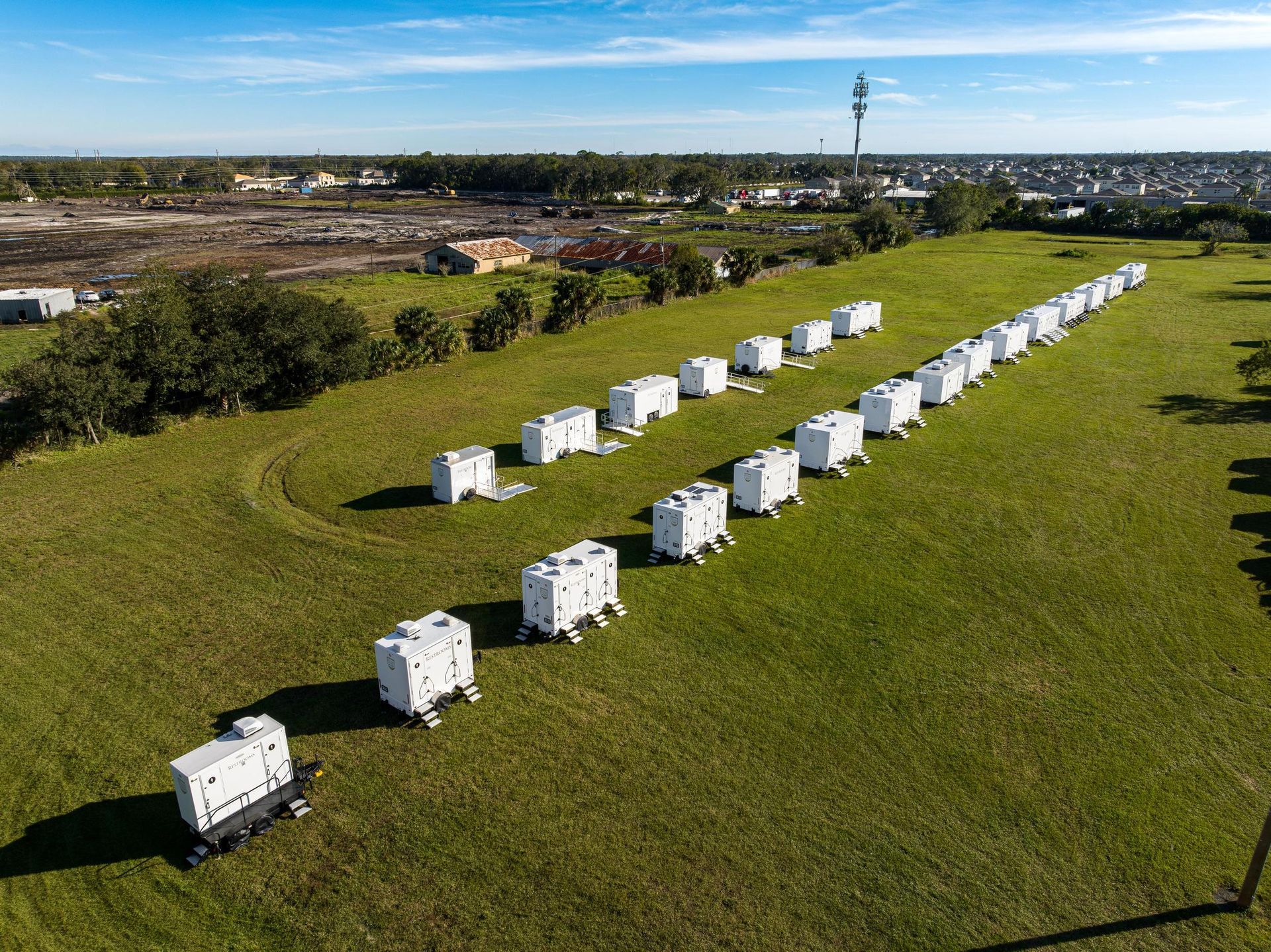 An aerial view of a row of white trailers in a grassy field