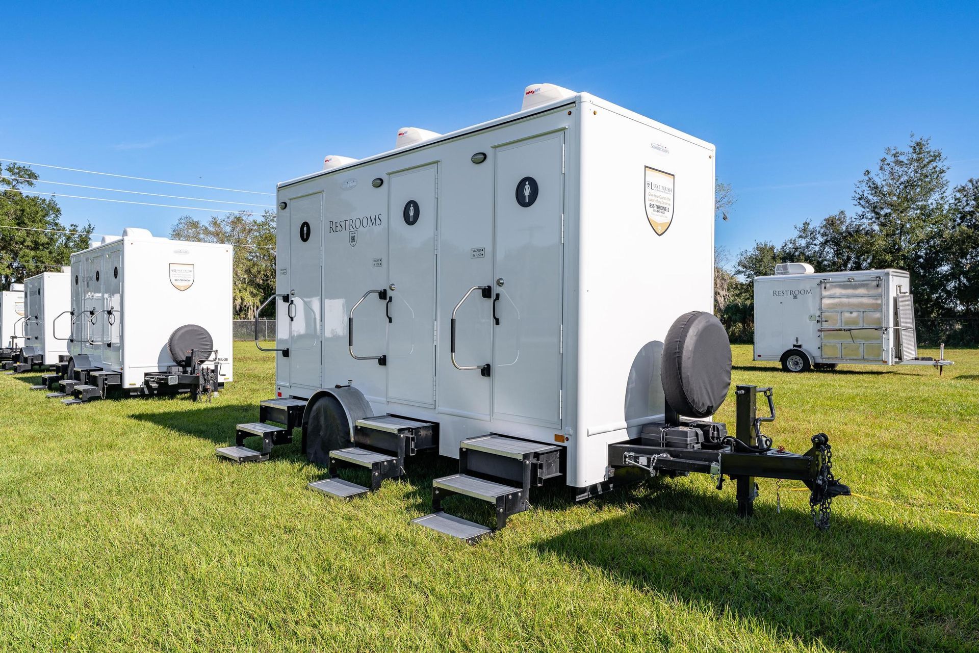 A row of white trailers are parked in a grassy field