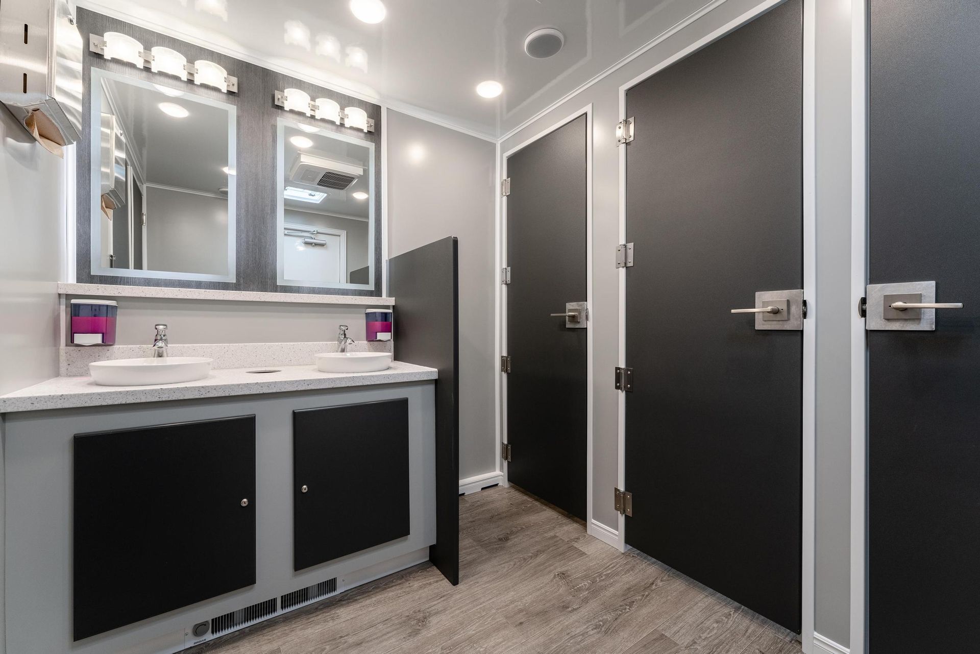 A bathroom with two sinks, two mirrors, and black doors