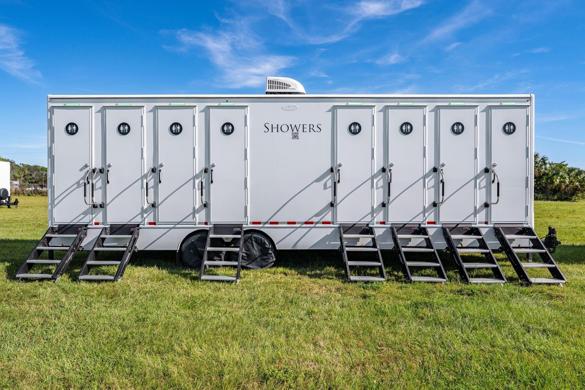 A white trailer with stairs attached to it is parked in a grassy field