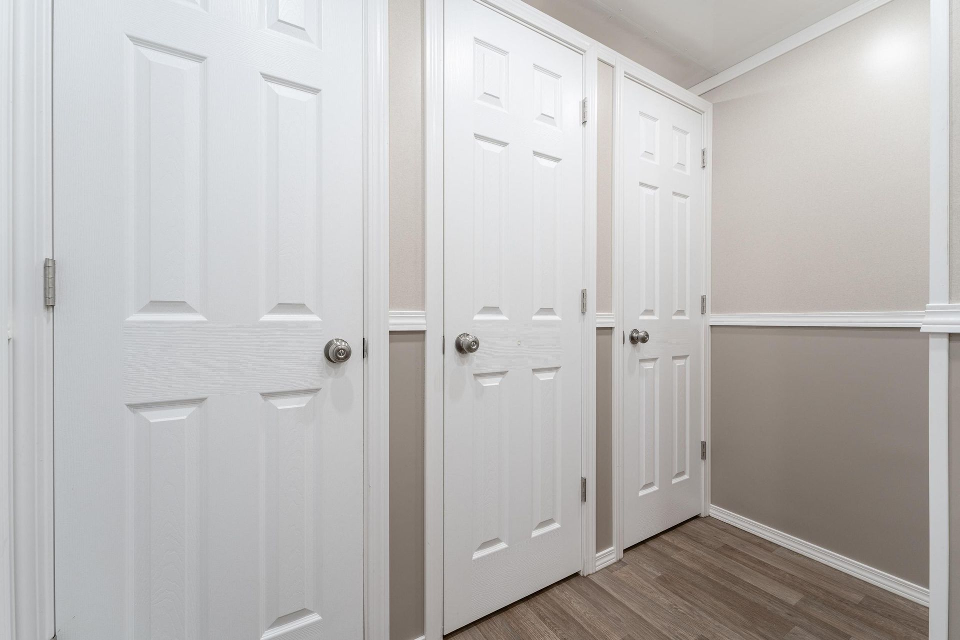 A hallway with a lot of white doors and a wooden floor