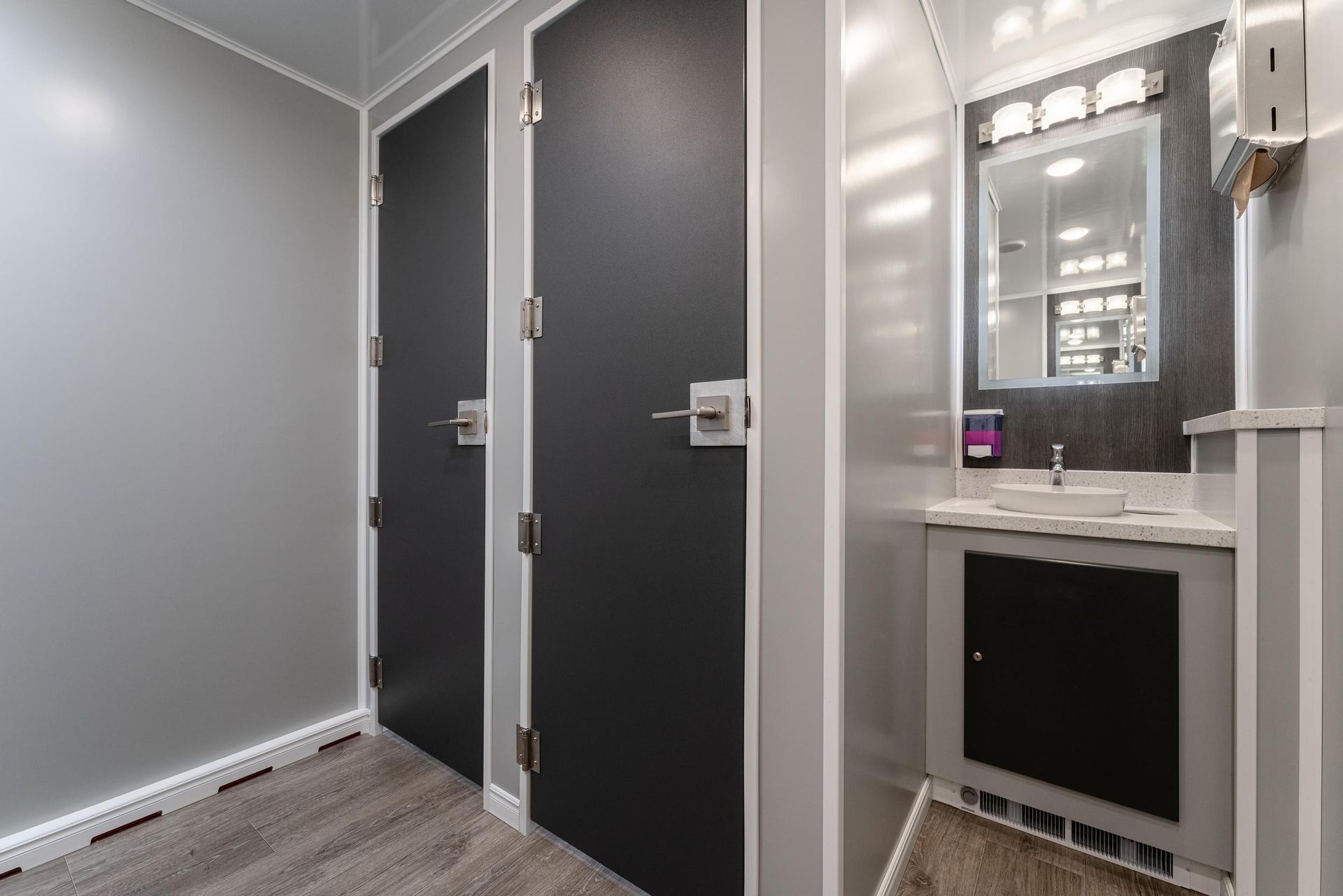 A bathroom with two stalls, a sink, and a mirror