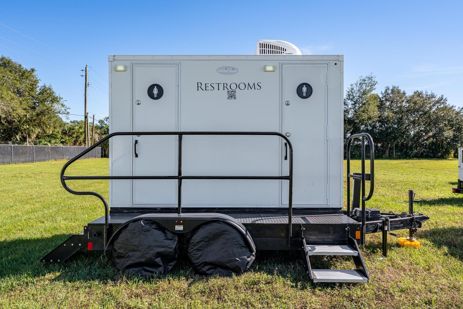 A white trailer with stairs attached to it is parked in a grassy field