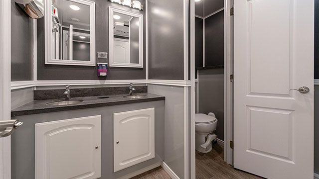 Modern bathroom vanity with mirrored cabinets, white cabinets, and an open door showing a toilet room.