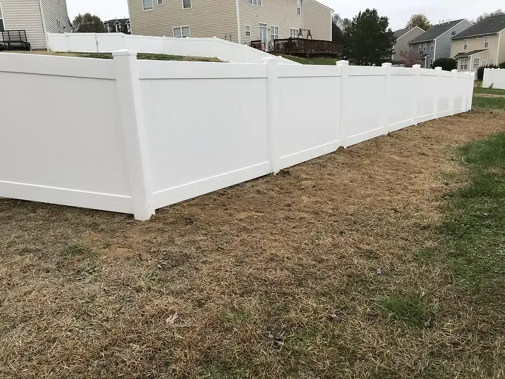 White vinyl fence borders a backyard with brown grass and a house in the background.