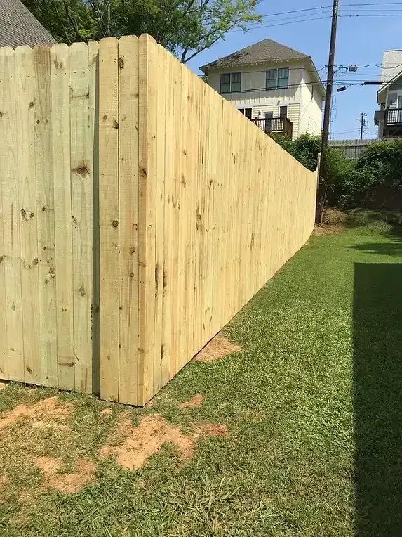 Wooden fence enclosing a grassy yard with a two-story house in the background.