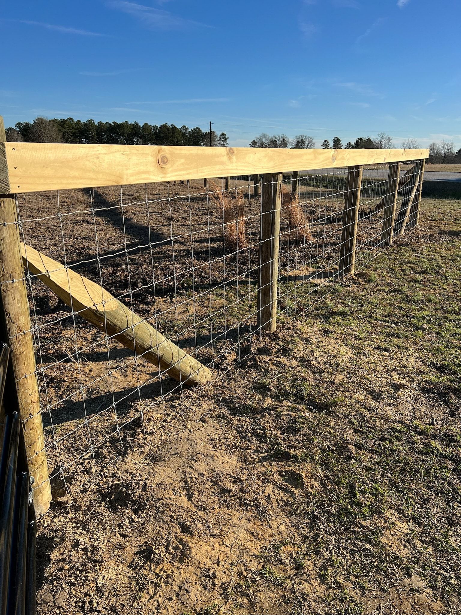 A fence constructed with wood posts and wire mesh, in a field under a blue sky.
