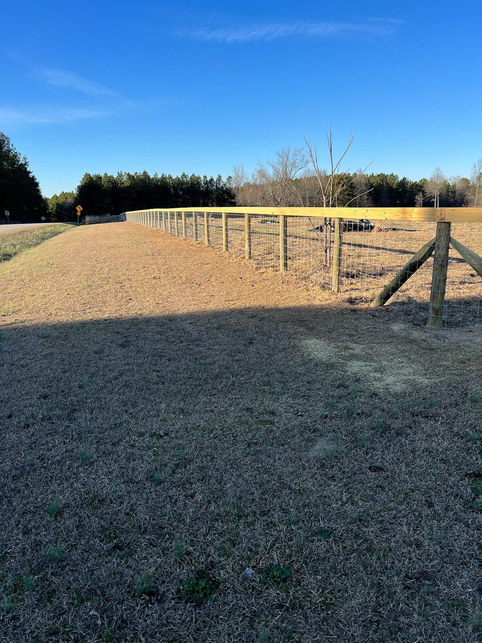 A newly built wooden fence in a grassy and gravelly field under a blue sky.