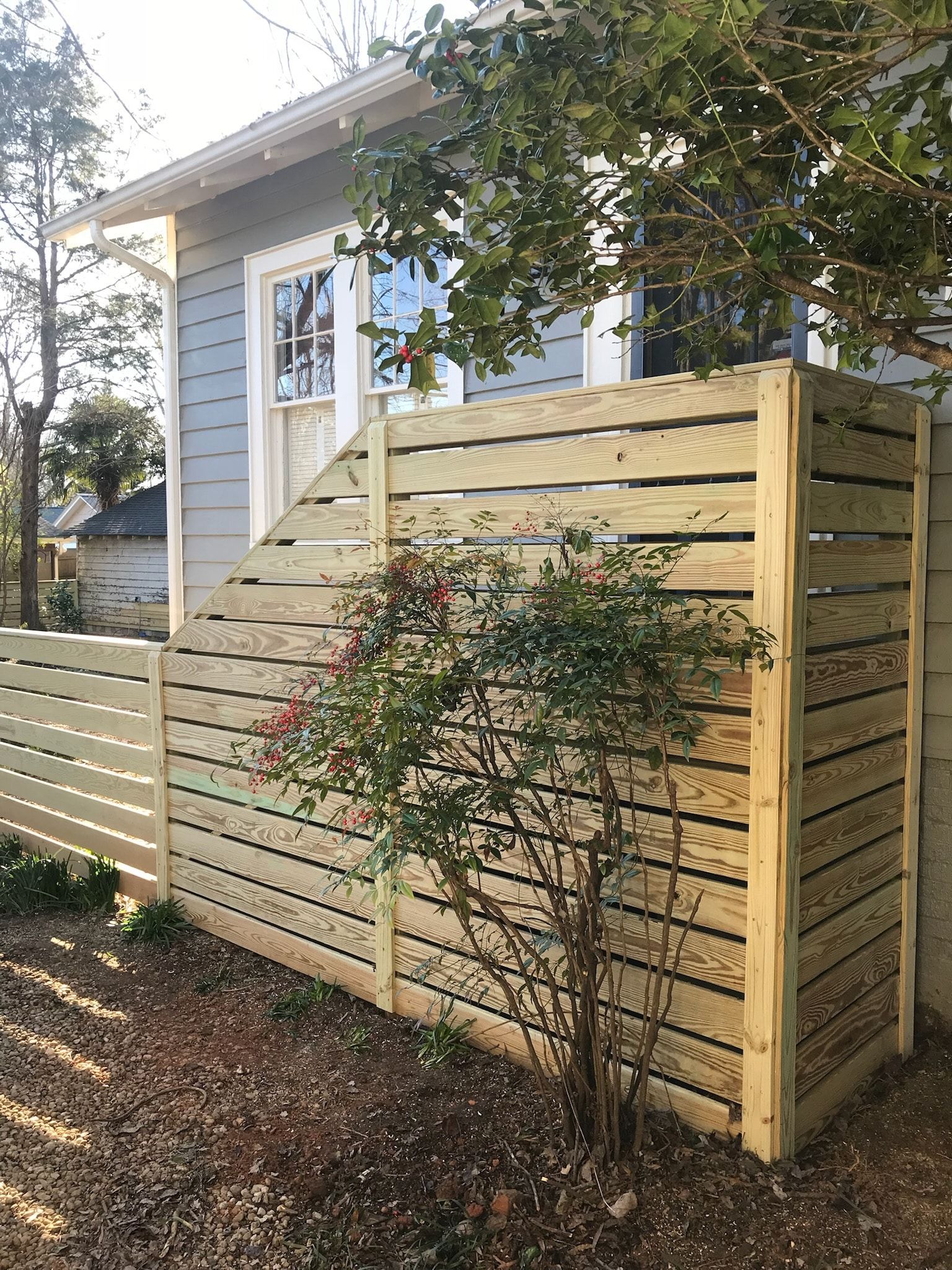 Wooden fence surrounds a small yard next to a blue house. A bush grows inside the fence.