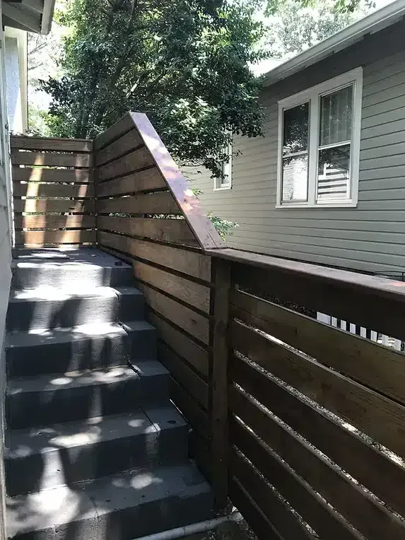 Outdoor stairway with wooden fence and light-colored house in the background.