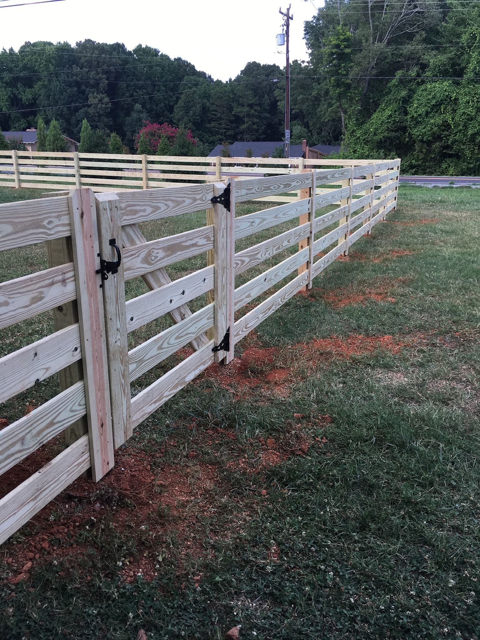 Wooden fence with two gates in a grassy yard, trees in the background.