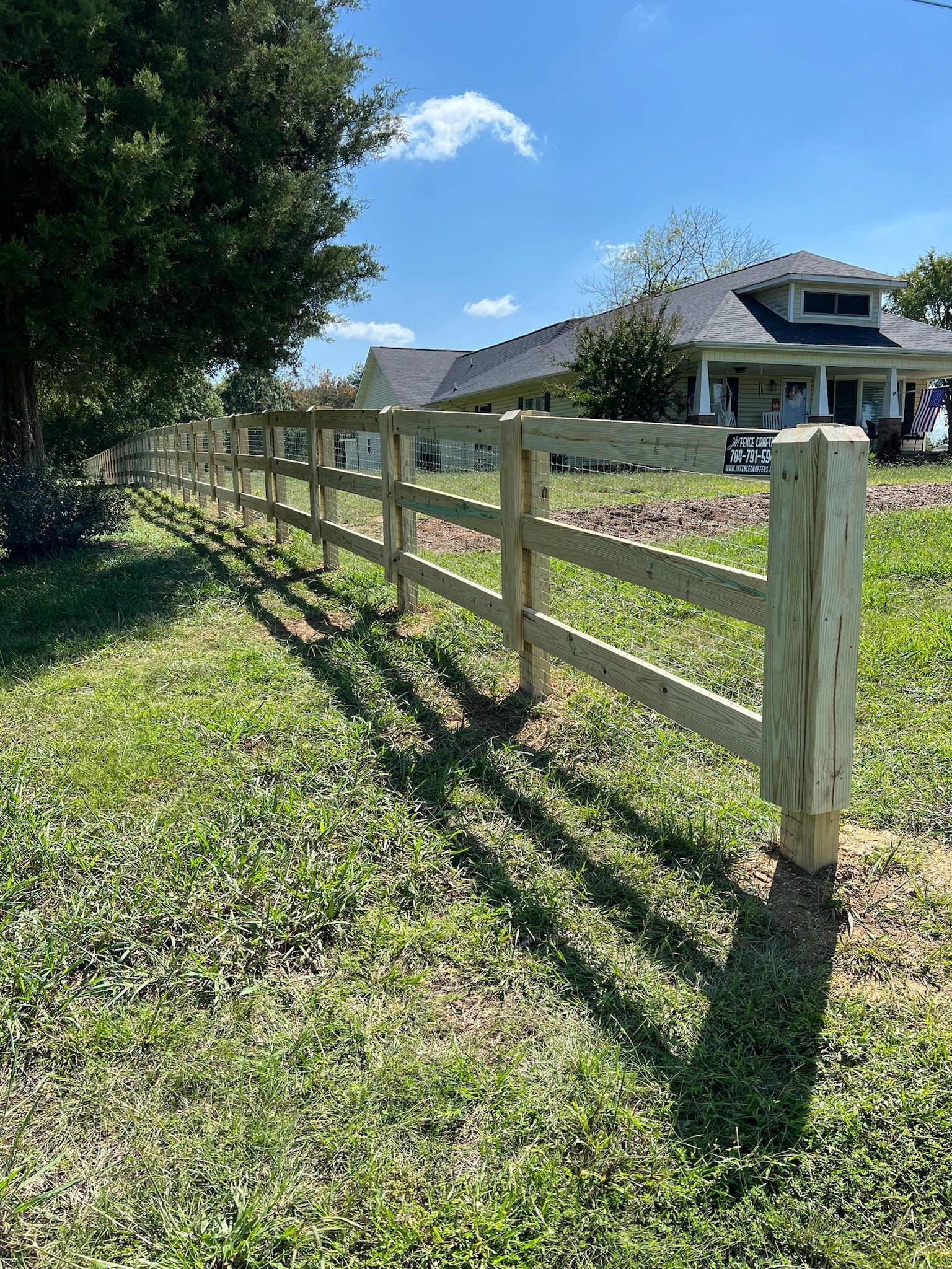 Wooden fence in grassy yard in front of a house on a sunny day.