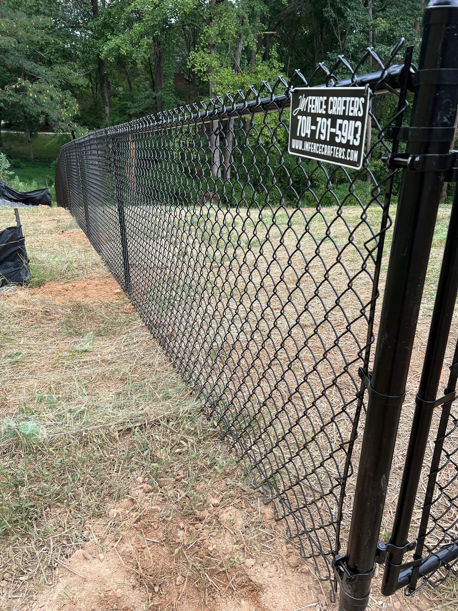 Black chain-link fence with black posts topped with barbs, outdoors in front of trees.