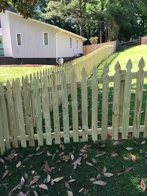Wooden picket fence in a grassy yard, leading alongside a light-colored building.