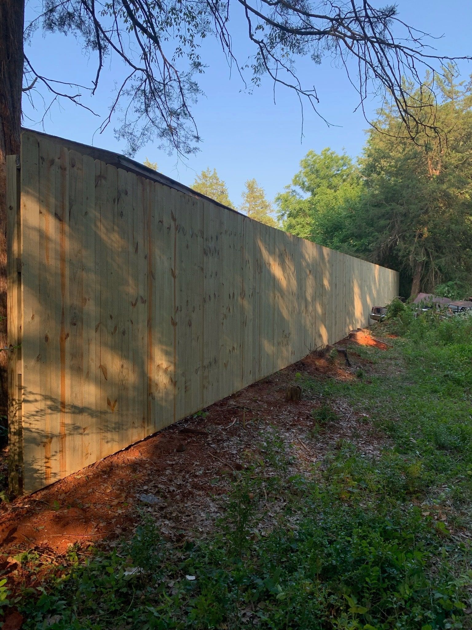 Wooden fence along a wooded area with sunlight casting shadows.