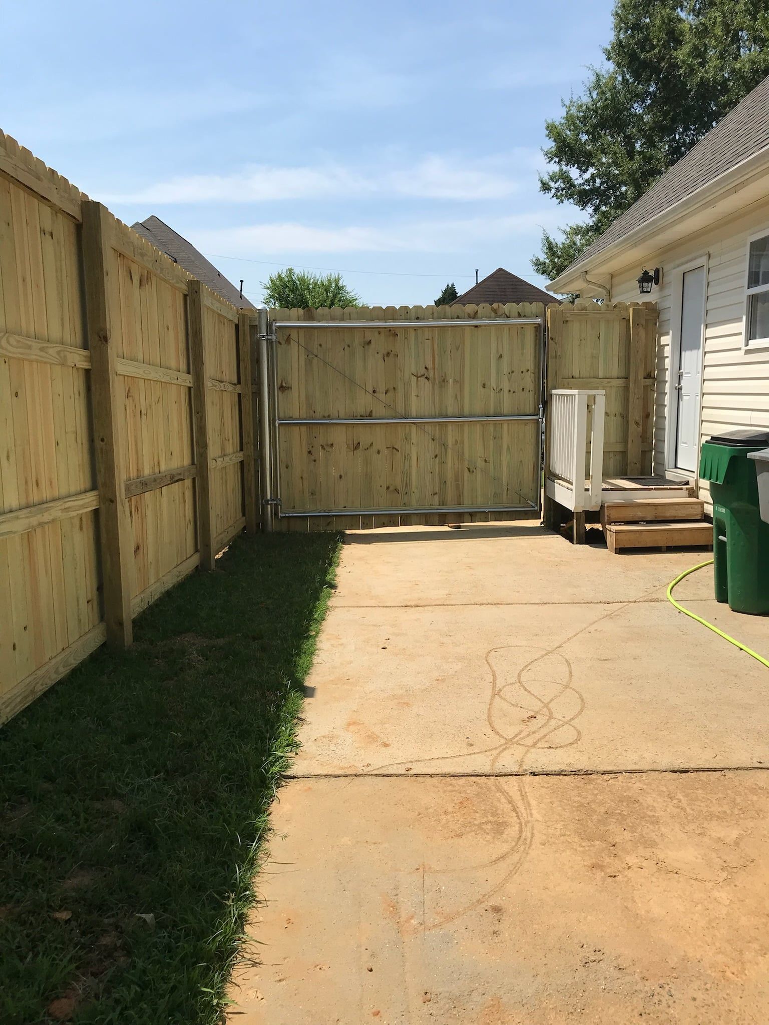 Wooden fence and gate enclose a concrete driveway leading to a back door.