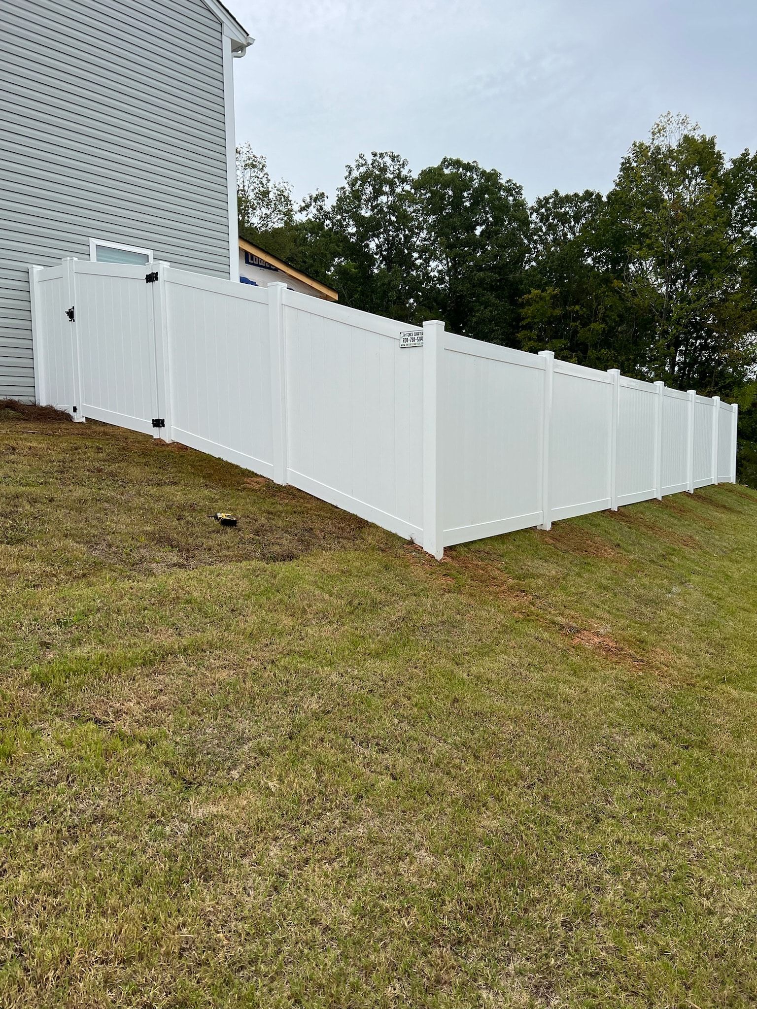 White vinyl fence along a grassy hill next to a white house.