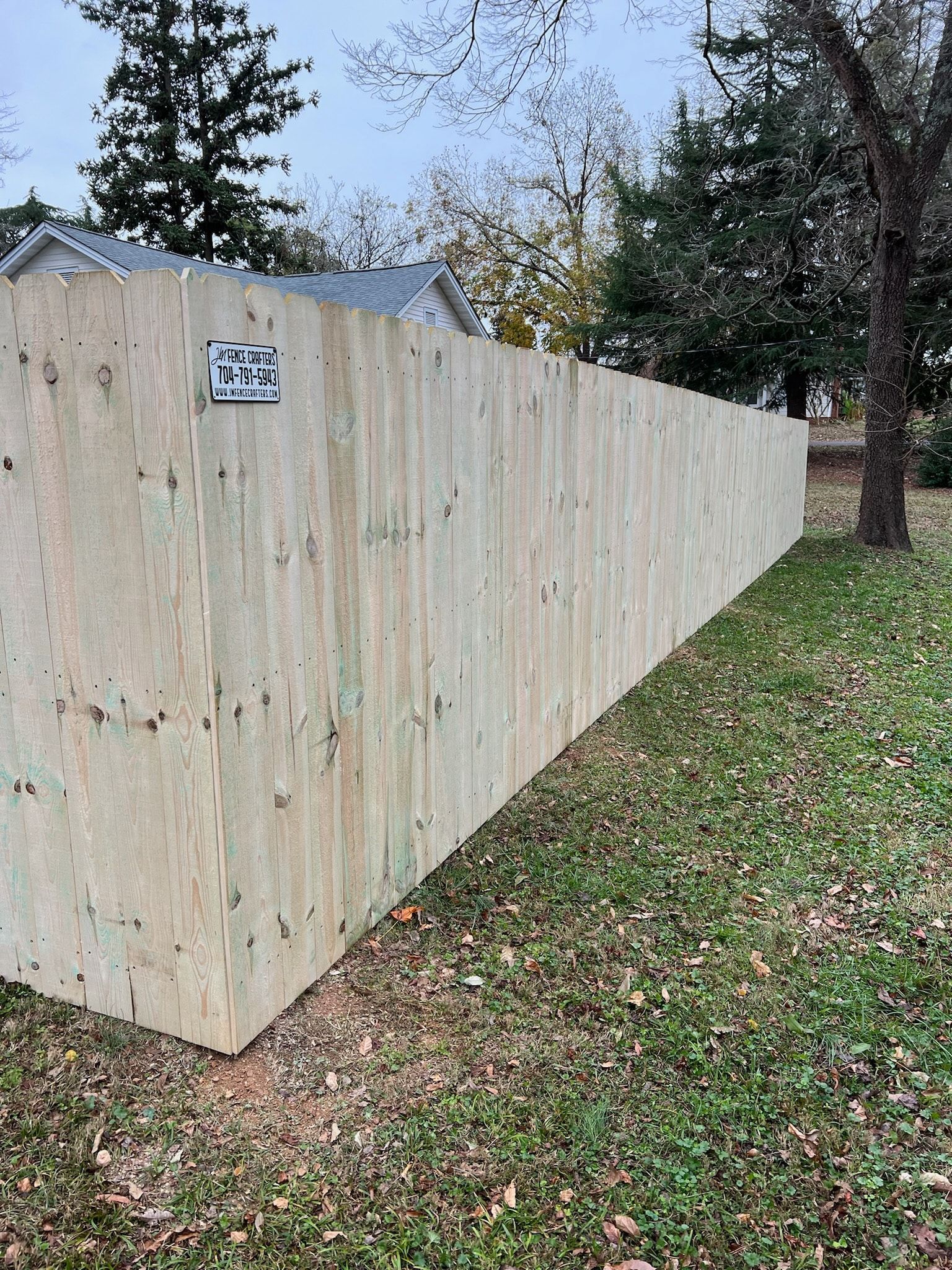 Wooden fence in a yard, with a grassy area and some trees in the background.