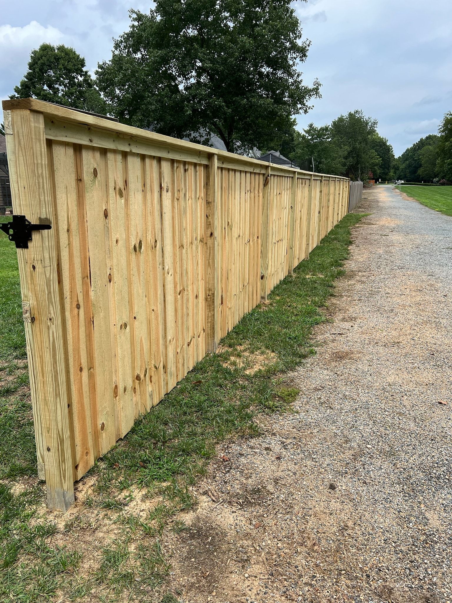 Wooden fence bordering a gravel path. Green grass and trees are visible in the background.