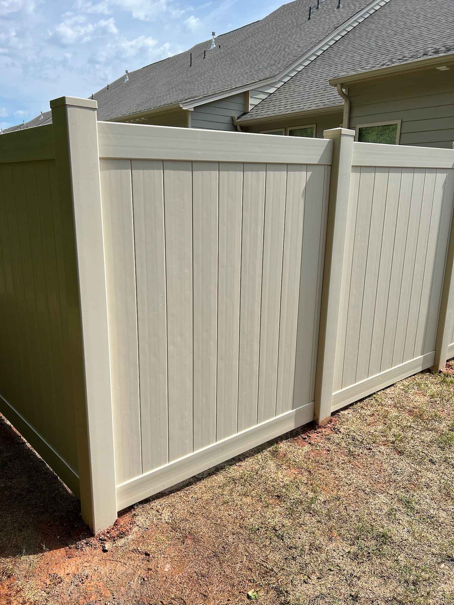 Tan vinyl privacy fence with solid and decorative panels in a yard, houses in background.