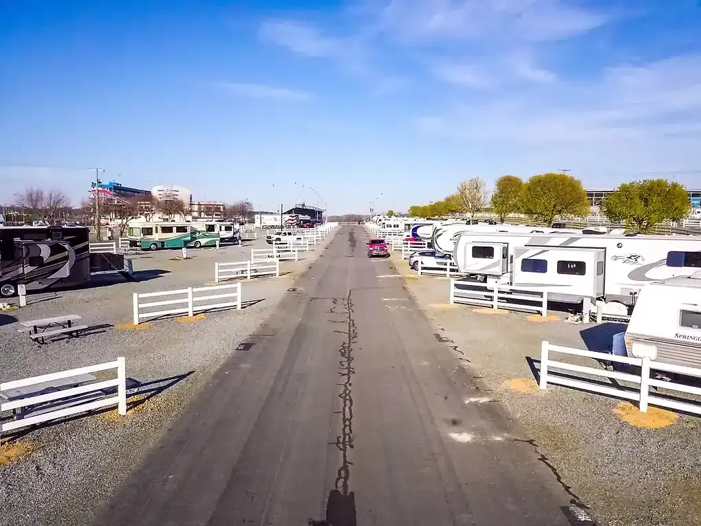 RV park with RVs parked on either side of a road, bright blue sky overhead.