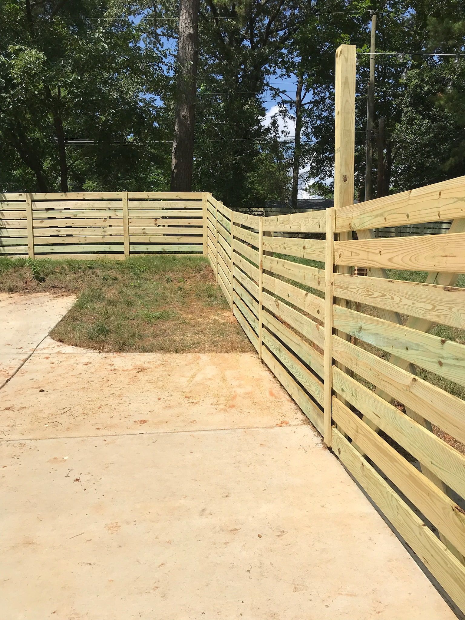 Wooden horizontal slat fence in a yard, curving towards trees.