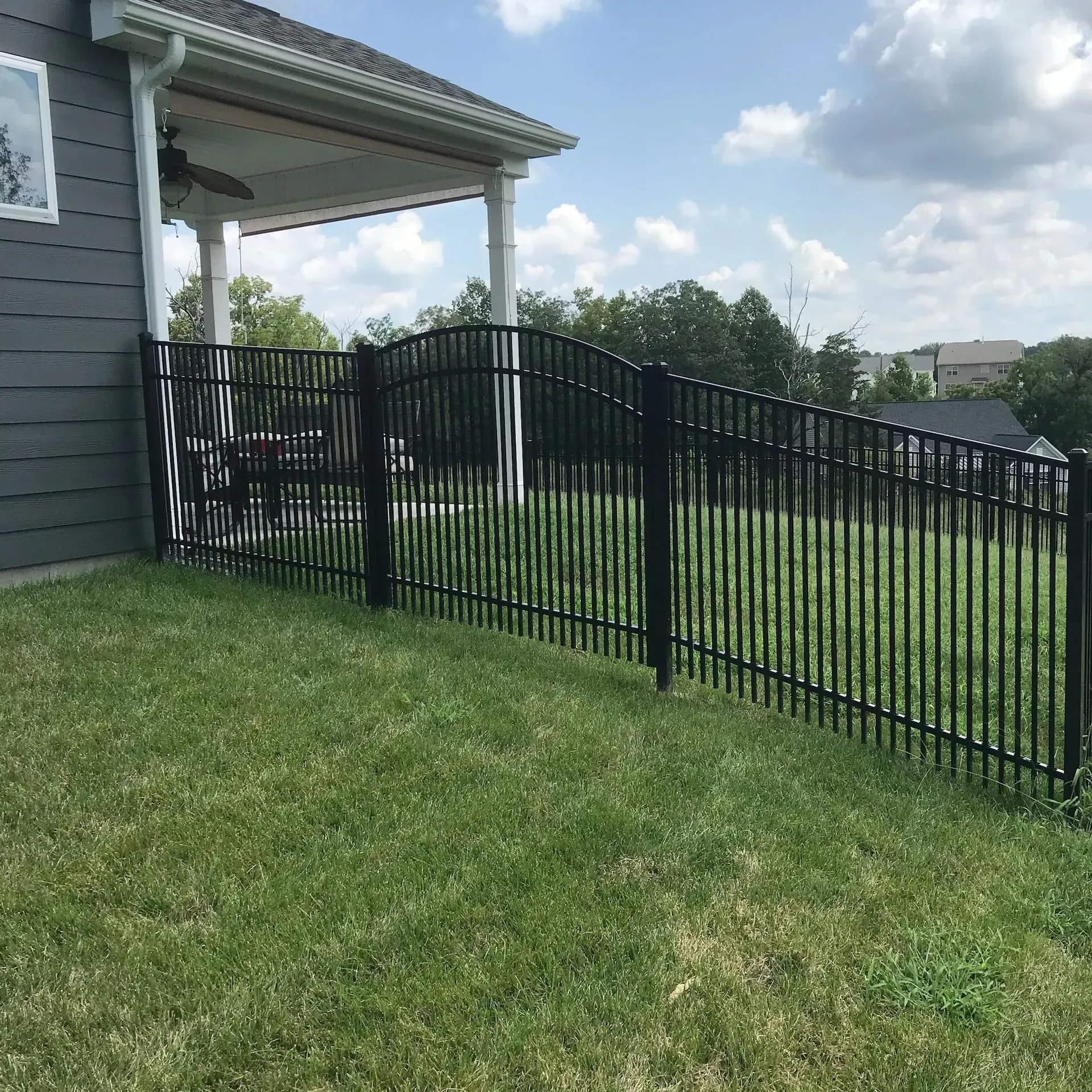 Black metal fence on a grassy slope, next to a house with a porch.