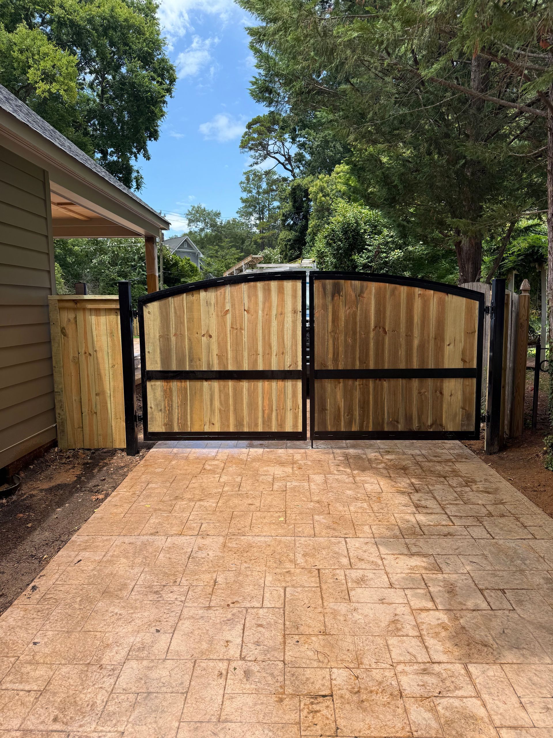 Wooden double gate with black metal frame on a stamped concrete driveway.