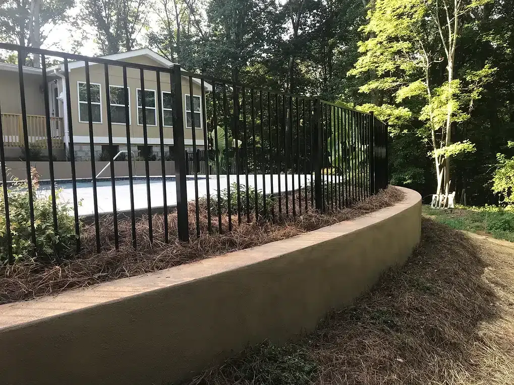 Black metal fence atop a tan retaining wall in front of a house.