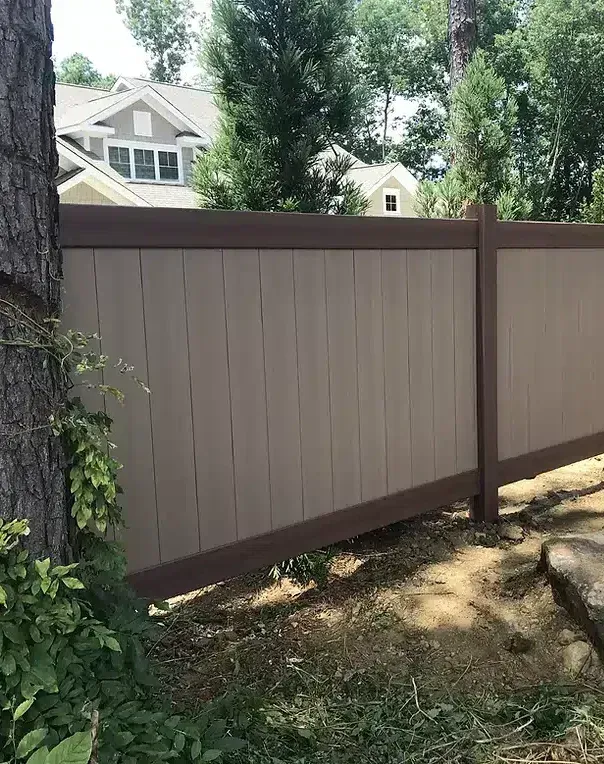 Tan and brown privacy fence in a yard, with houses and trees in the background.