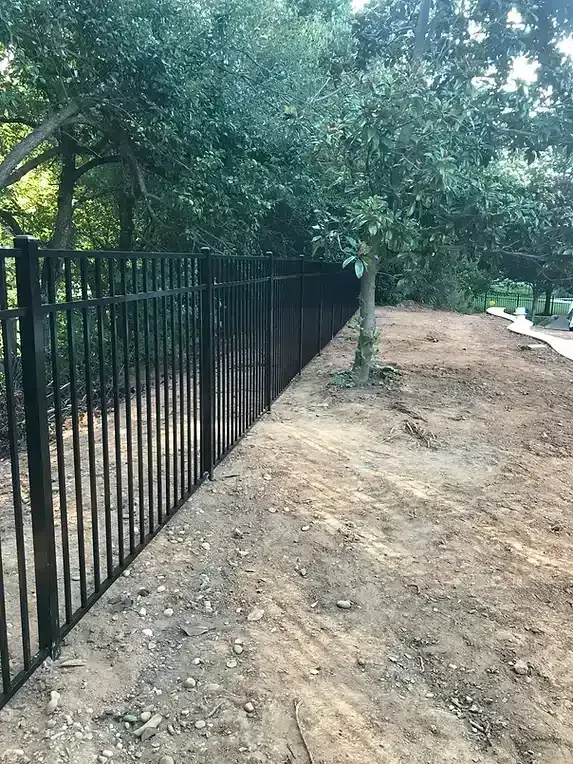 Black metal fence bordering a dirt path, with trees in the background.