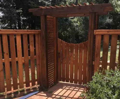 Wooden fence with gate under a pergola. The gate and fence are stained brown.