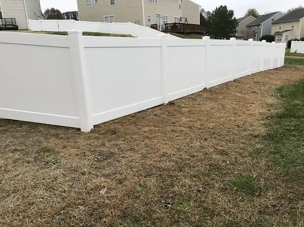 White vinyl fence bordering brown grass in a residential yard.