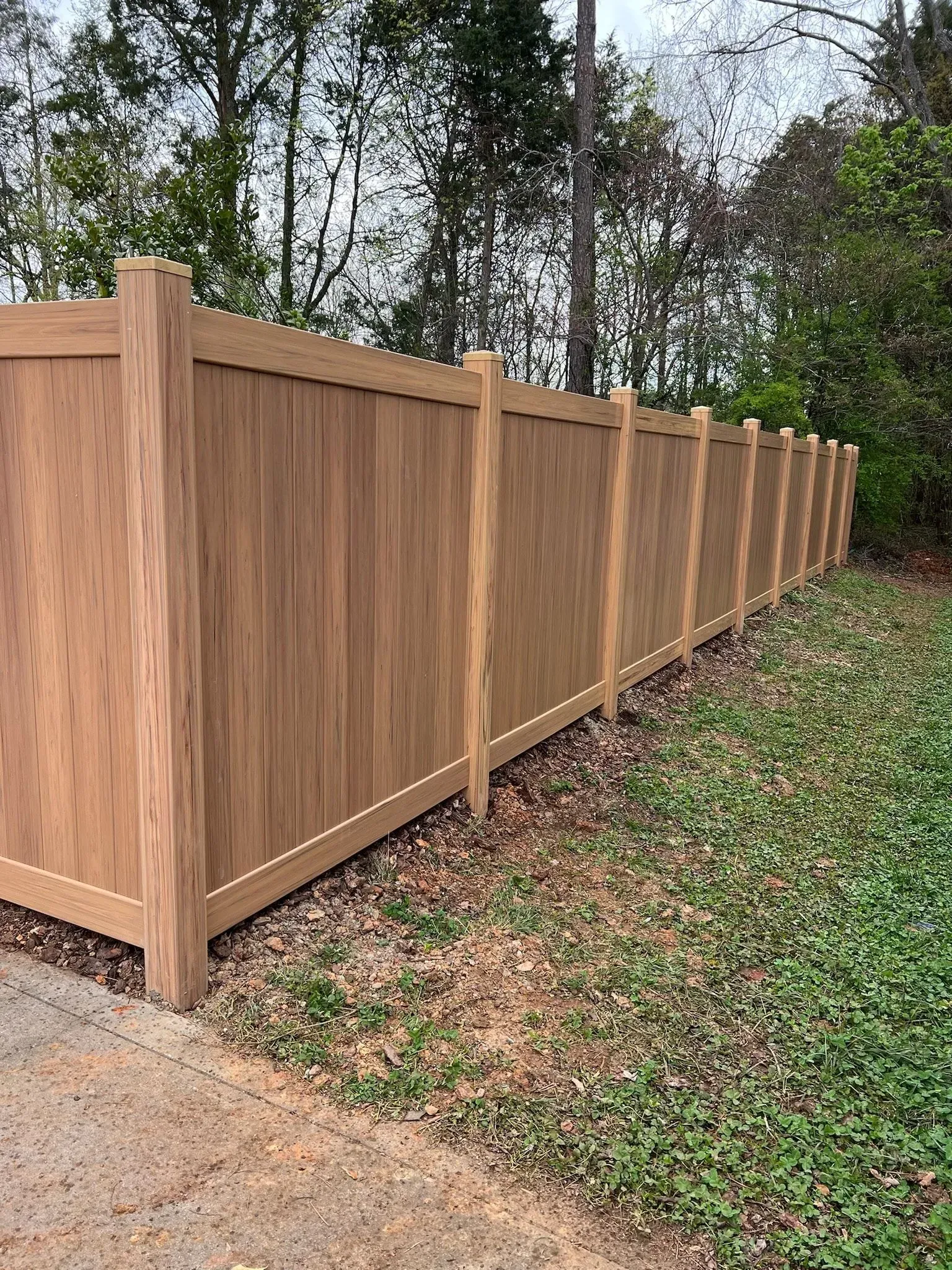 Brown wooden privacy fence in a yard, trees in the background.