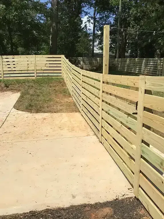 Wooden horizontal slat fence alongside a concrete path, sunny day.
