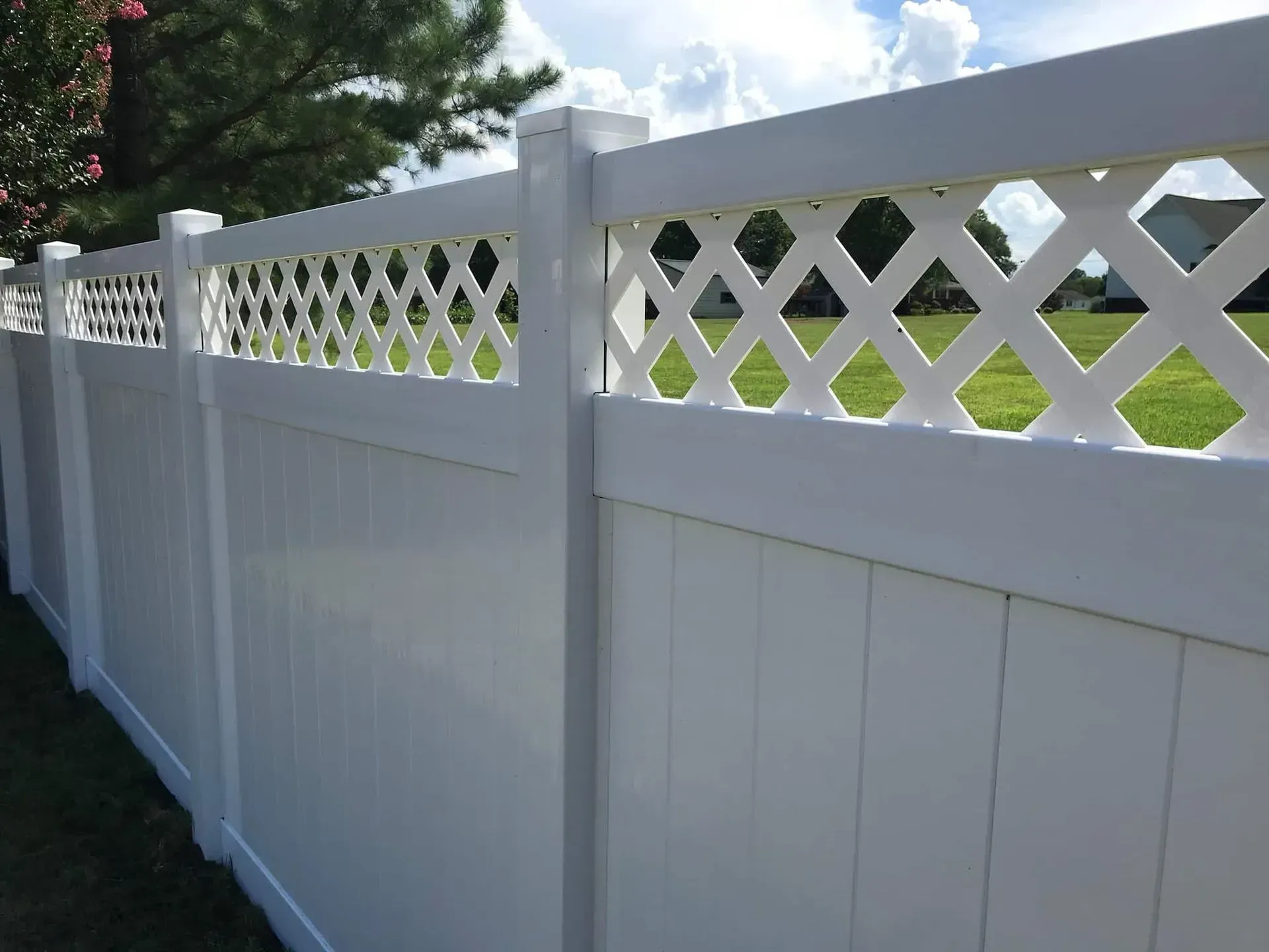 White vinyl privacy fence with lattice top, in a grassy yard on a sunny day.