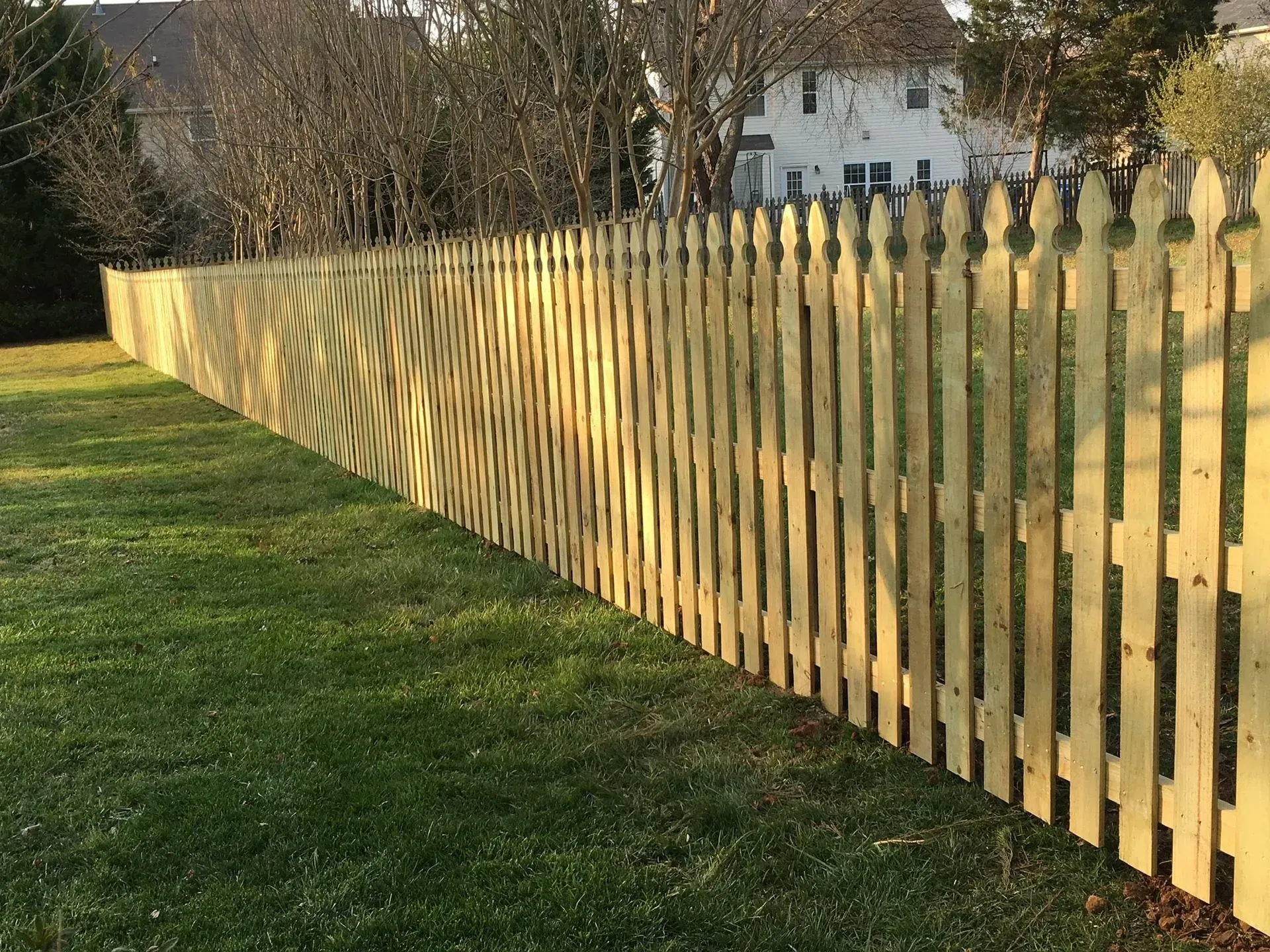 Wooden picket fence in a yard, casting shadows on the grass.