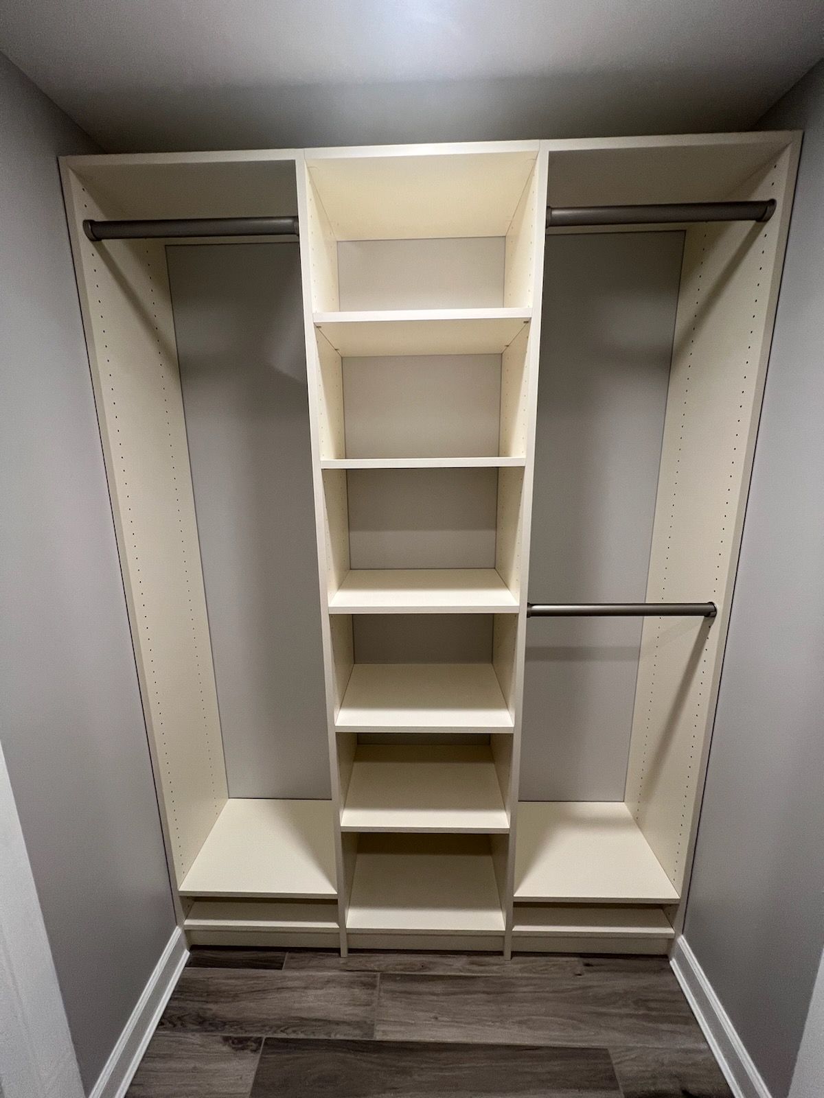 Built-in closet with cream-colored shelves and rods. Center has a tall, vertical shelf unit with several shelves.