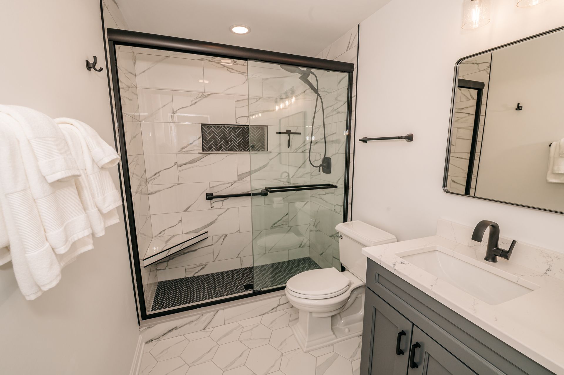 Modern bathroom with a glass shower, white marble tiles, gray vanity, and a toilet.